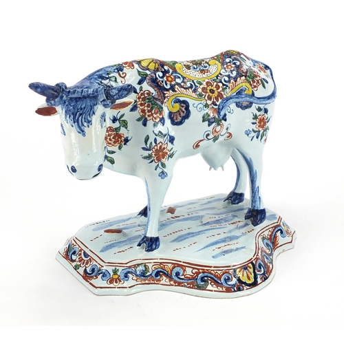 469 - Delft pottery cow mounted on grassy base, hand painted with flowers, initials to base, 17cm high