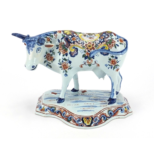 469 - Delft pottery cow mounted on grassy base, hand painted with flowers, initials to base, 17cm high