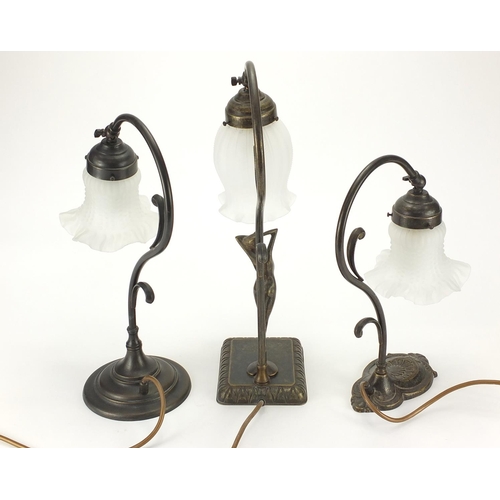 142 - Three bronzed metal table lamps with frosted glass shades including one with nude figurative support... 