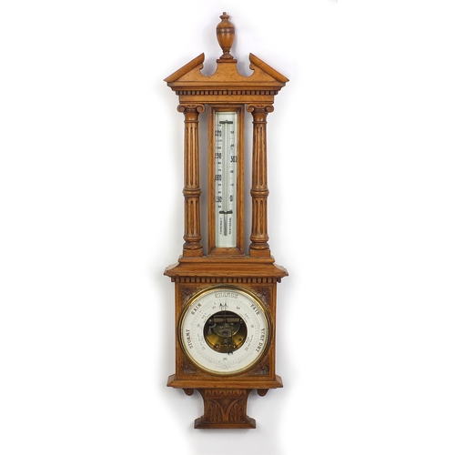 1145 - Oak aneroid barometer thermometer, with broken arch pediment and urn finial, 95cm in length