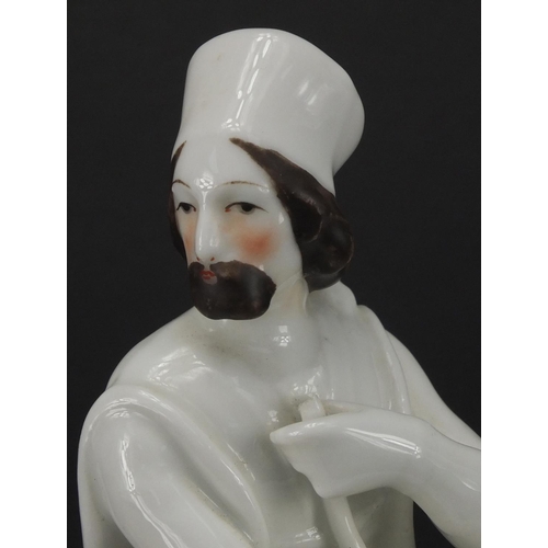 614 - Blanc du chine porcelain model of a Russian gentleman seated on a cushion smoking a pipe beside bask... 