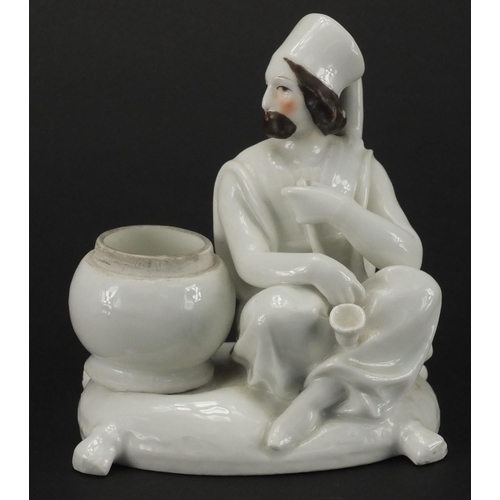 614 - Blanc du chine porcelain model of a Russian gentleman seated on a cushion smoking a pipe beside bask... 