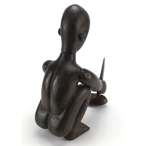 570 - African tribal interest wood carving of a crouching figure carving a nut with articulated arms, 37cm... 