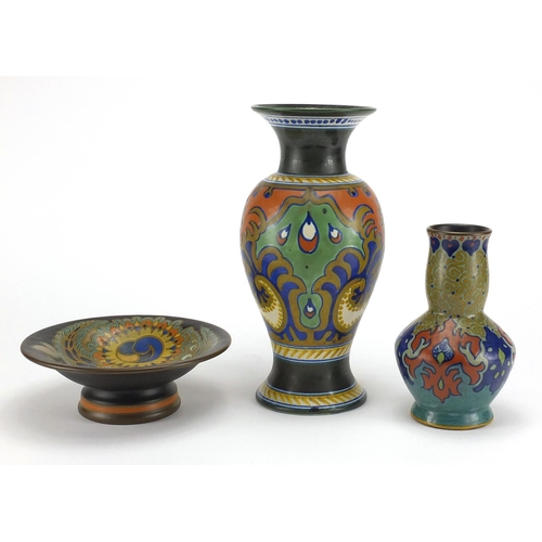 670 - Two Dutch art pottery vases and a tazza by Gouda, each hand painted with stylised flowers and with f... 