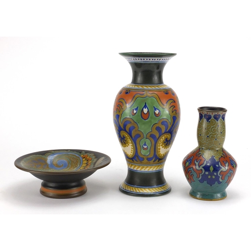 670 - Two Dutch art pottery vases and a tazza by Gouda, each hand painted with stylised flowers and with f... 