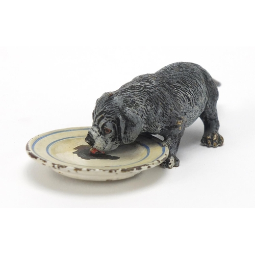 5 - Austrian cold painted bronze dog licking a plate, stamped Geschutzt to the base, 9cm in length