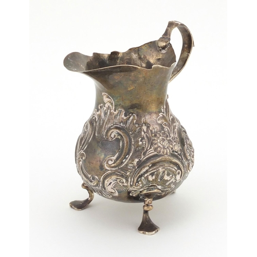 659 - Georgian silver three footed cream jug with embossed decoration, 12cm high, approximate weight 133.0... 