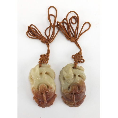 433 - Three Chinese russet and green jade pendants including a pair carved as mythical animals, with cords... 