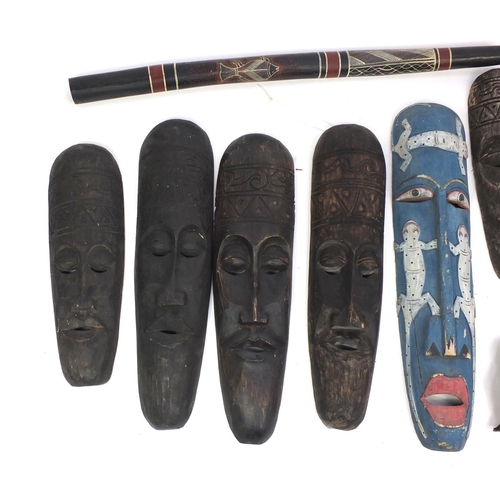 643 - Nine tribal interest carved wooden wall masks and a didgeridoo, the largest mask 88cm in length