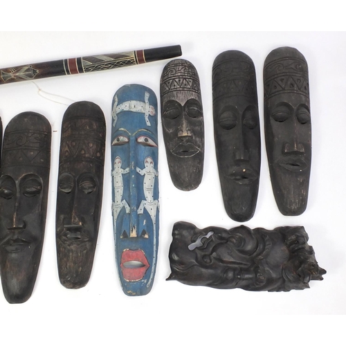 643 - Nine tribal interest carved wooden wall masks and a didgeridoo, the largest mask 88cm in length