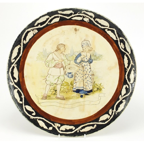 577 - Minton's pottery charger hand painted with two figures before a town, within a foliate border, impre... 