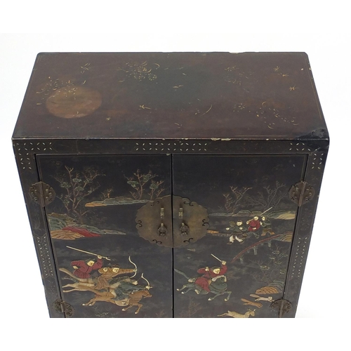23 - Oriental lacquered cabinet with two panelled doors, hand painted and decorated in relief with huntsm... 