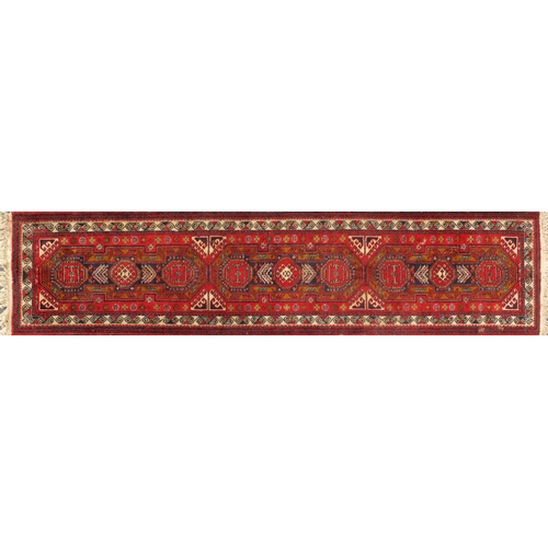 2028 - Rectangular Persian carpet runner having an all over geometric design onto a red ground, 330cm x 78c... 