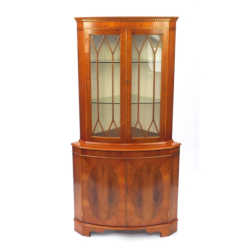 43 - Yew corner cabinet, fitted with a pair of glazed doors enclosing two glass shelves, above two cupboa... 