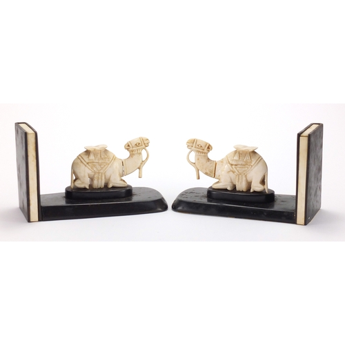 63 - Pair of African hardwood bookends, each mounted with a carved ivory camel, each 18.5cm wide