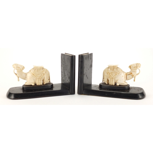 63 - Pair of African hardwood bookends, each mounted with a carved ivory camel, each 18.5cm wide