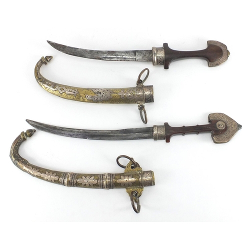 588 - Two Islamic daggers with brass sheaths having silver inlay, engraved with stylised scrolls, the larg... 