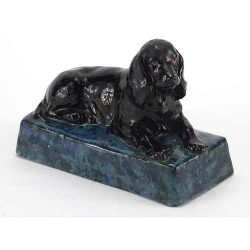 944 - Stella Crofts pottery model of a recumbent spaniel, with a black and mottled blue glaze, incised Ste... 