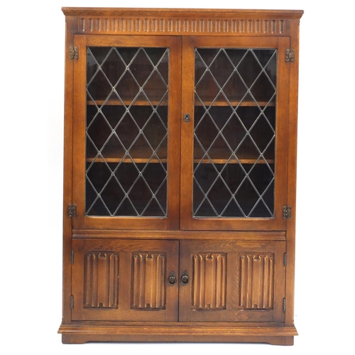 23 - Oak linen fold bookcase, fitted with a pair of leaded glass doors, above a pair of cupboard doors, 1... 