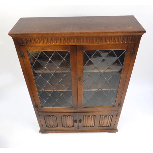 23 - Oak linen fold bookcase, fitted with a pair of leaded glass doors, above a pair of cupboard doors, 1... 