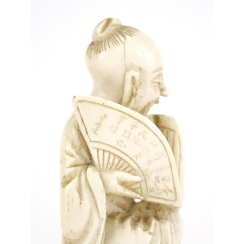 412 - Chinese ivory carving of a seated man holding a fan with calligraphy, raised on a carved hardwood st... 