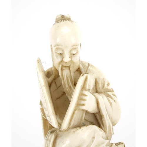 412 - Chinese ivory carving of a seated man holding a fan with calligraphy, raised on a carved hardwood st... 