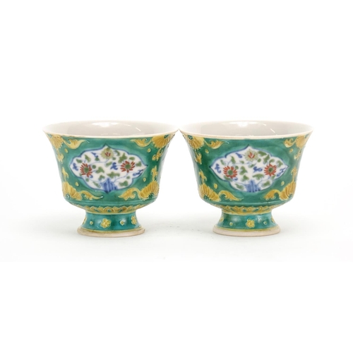 299 - Pair of Chinese Doucai porcelain stem cups, each hand painted with panels of flowers onto a green gr... 