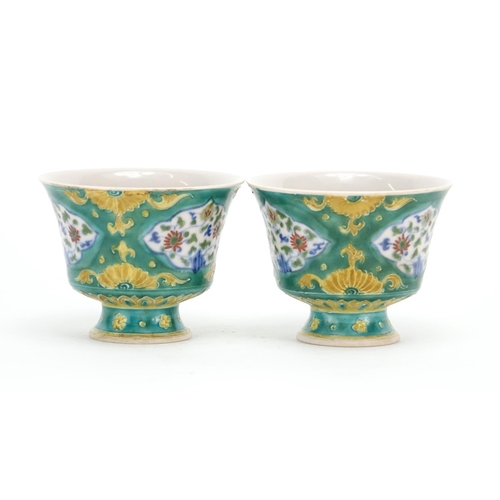 299 - Pair of Chinese Doucai porcelain stem cups, each hand painted with panels of flowers onto a green gr... 