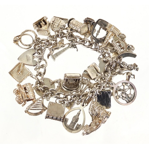 2457 - Silver charm bracelet, with large selection of mostly silver charms including windmill, wagon, tram ... 