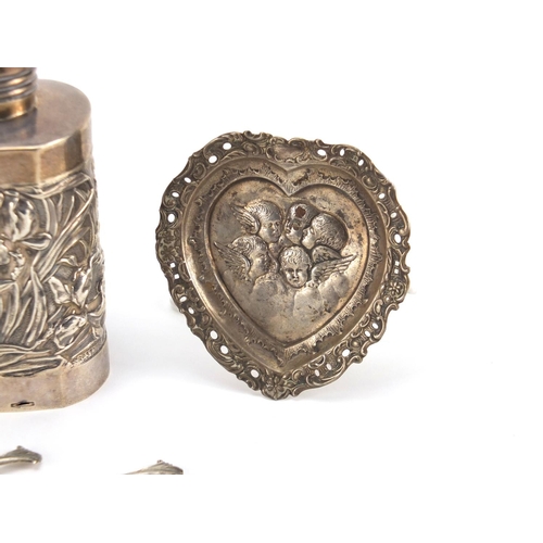 2386 - Silver objects comprising an aesthetic bottle holder, heart shaped pin dish, two teaspoons and a cut... 