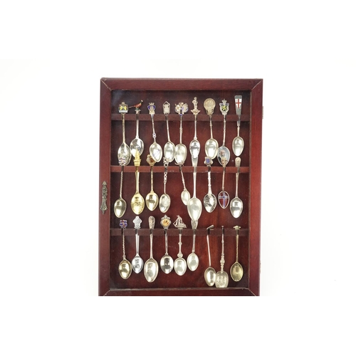 2251 - Silver and white metal souvenir teaspoons, some with enamelled decoration, housed in a mahogany disp... 