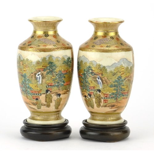 313 - Pair of Japanese Satsuma pottery vases raised on hardwood stands, hand painted with figures, flowers... 