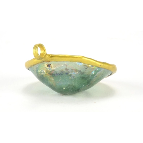 389A - Iridescent Roman glass fragment housed in a gilt painted pendant mount, 5.8cm high