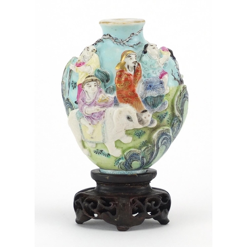 417 - Chinese porcelain relief snuff bottle raised on a carved hardwood stand, hand painted in the famille... 