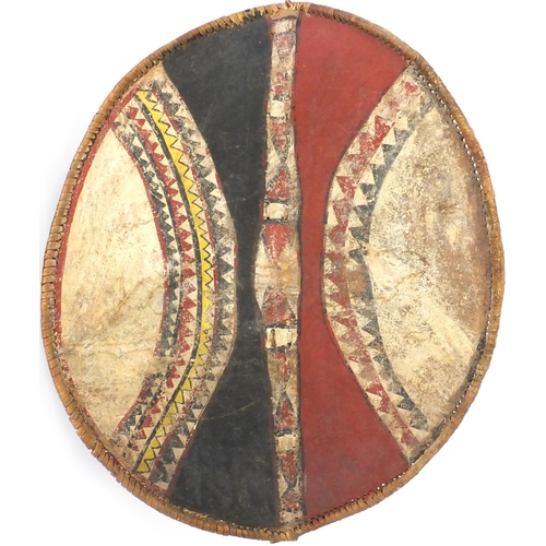 663 - Tribal interest Maasai shield and spear, the shield hand painted with a geometric decoration, the sh... 