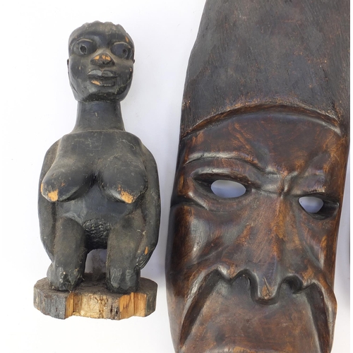 665 - African tribal carvings including two face masks and a fertility figure, the largest 62cm in length