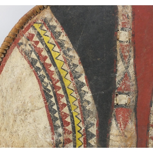573 - Tribal interest Maasai shield and spear, the shield hand painted with a geometric decoration, the sh... 