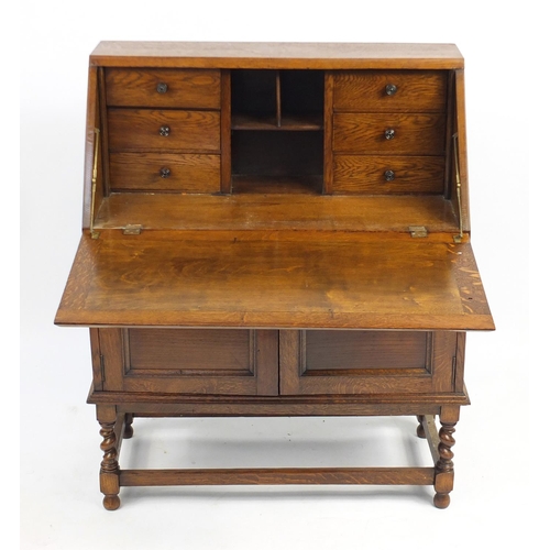 102 - Oak bureau, the fall enclosing a fitted interior above a pair of cupboard doors and barley twist leg... 