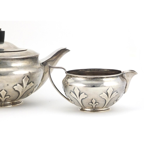 520 - Arts & Crafts style silver three piece tea service embossed with stylised motifs, the teapot with eb... 