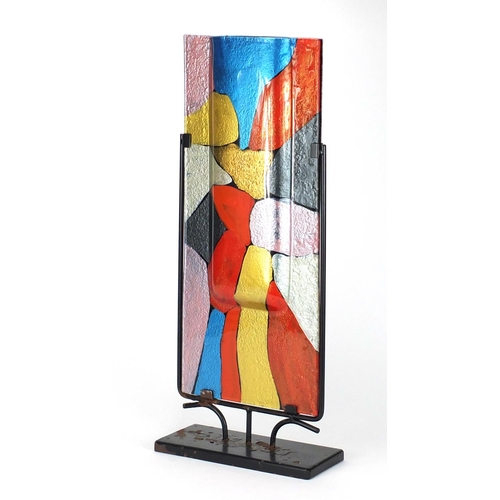 2325 - Modernist painted glass sculptural vase housed in a metal stand, overall 61cm high