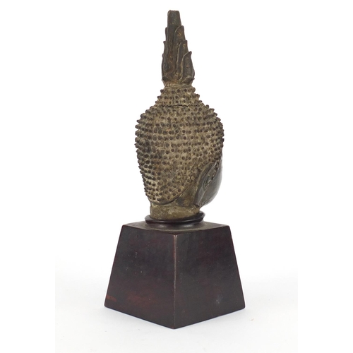 522 - Thai patinated bronze head of a deity raised on a square tapering hardwood stand, overall 22cm high