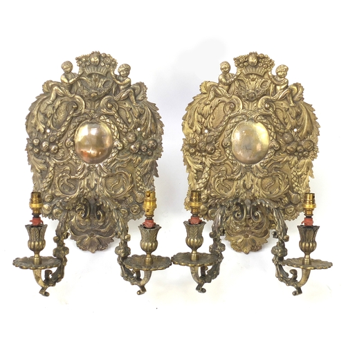 2111 - Pair of silver plated two branch wall sconces, decorated with putti and swags, each 36cm high