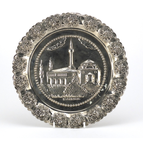 699 - Iranian silver coloured metal plate, embossed with a church within a foliate border, 28cm in diamete... 