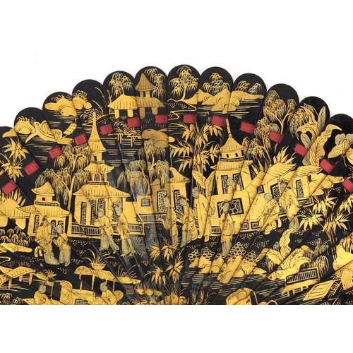 39 - Chinese black lacquer fan gilded with figures amongst pagodas and a river landscape, 20cm in length