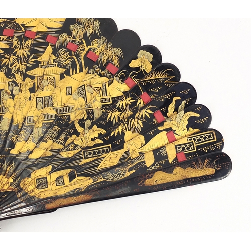 39 - Chinese black lacquer fan gilded with figures amongst pagodas and a river landscape, 20cm in length