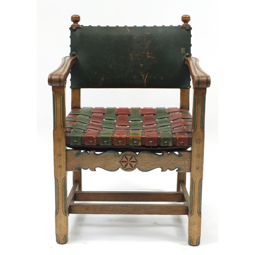 2046 - Carved oak open arm chair with red and green leather strap seat, 85cm high