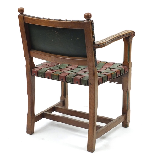 2046 - Carved oak open arm chair with red and green leather strap seat, 85cm high