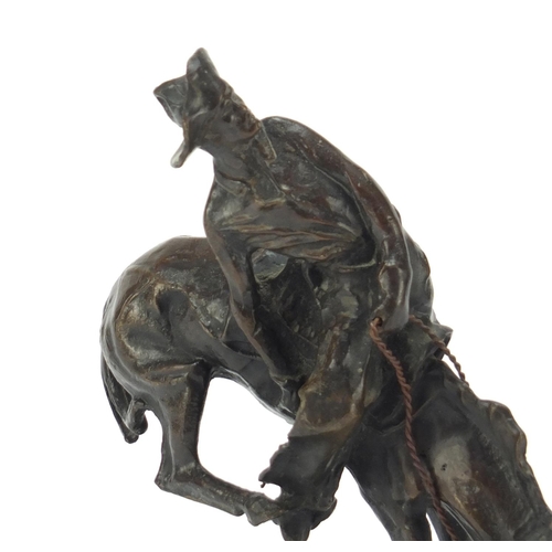 492 - Patinated bronze figure of a cowboy on horseback in the style of Frederick Remington, raised on an o... 