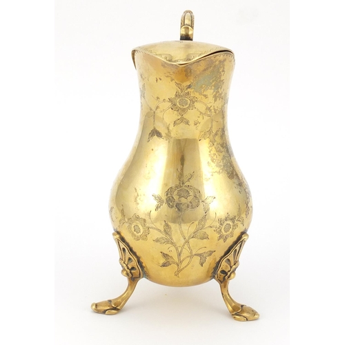 320 - Silver gilt water jug with hinged lid, the body engraved with flowers and raised on three hoof feet,... 