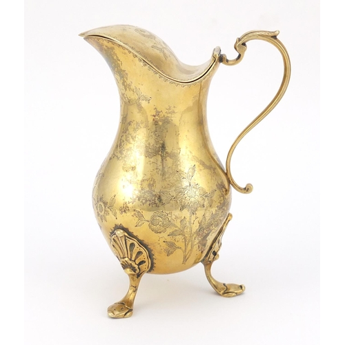 320 - Silver gilt water jug with hinged lid, the body engraved with flowers and raised on three hoof feet,... 